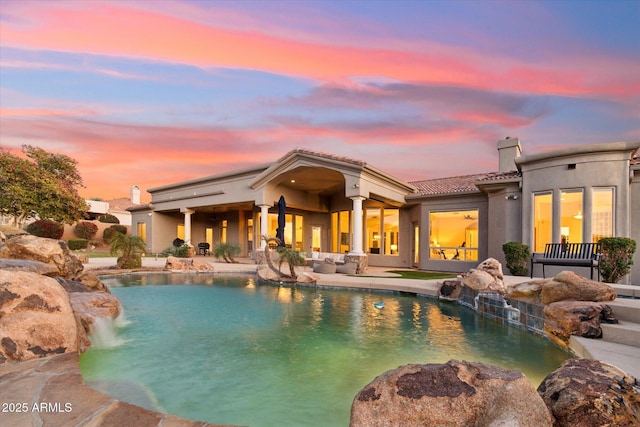 pool at dusk featuring pool water feature and a patio