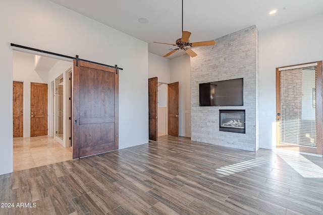 unfurnished living room with a high ceiling, ceiling fan, a barn door, light wood-type flooring, and a large fireplace