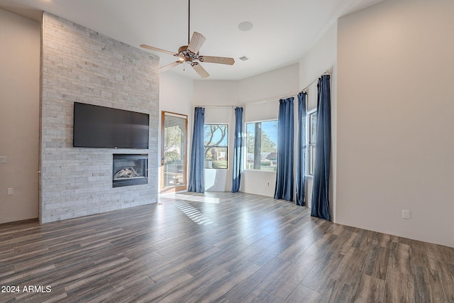 unfurnished living room with ceiling fan, a large fireplace, wood-type flooring, and a high ceiling