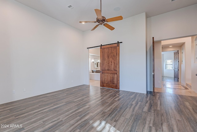 unfurnished bedroom featuring connected bathroom, ceiling fan, a high ceiling, a barn door, and wood-type flooring