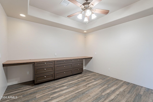 empty room featuring a tray ceiling, ceiling fan, dark wood-type flooring, and built in desk