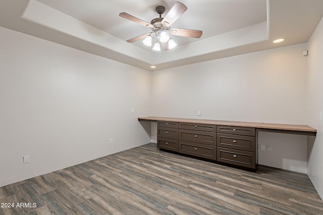 spare room featuring a raised ceiling, ceiling fan, built in desk, and dark hardwood / wood-style floors