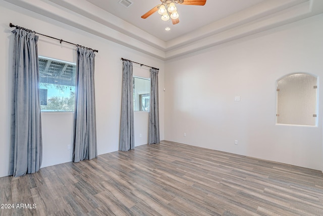 empty room with hardwood / wood-style flooring, ceiling fan, and a tray ceiling