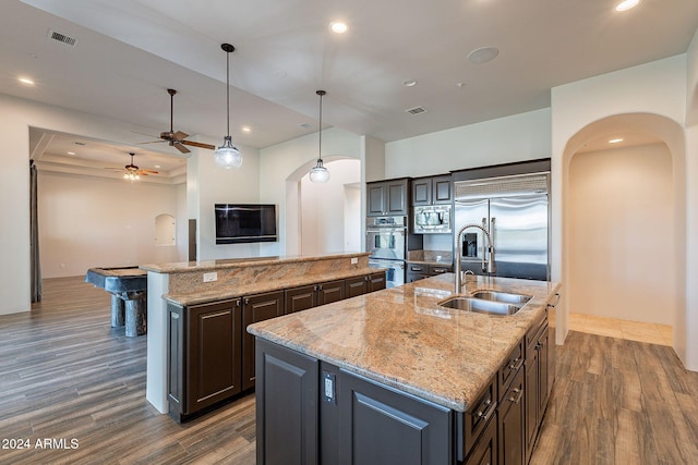 kitchen featuring built in appliances, dark brown cabinets, an island with sink, and hanging light fixtures