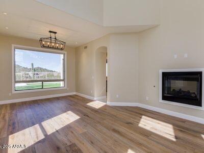 3634 N Desert Oasis, Mesa, AZ 85207 - unfurnished living room with wood finished floors, baseboards, a glass covered fireplace, arched walkways, and a chandelier