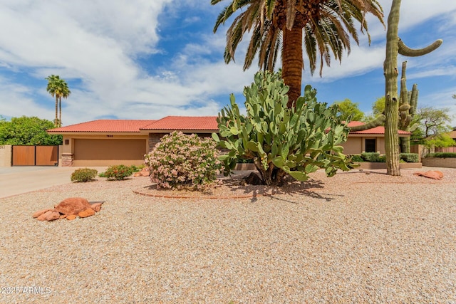 view of front facade with an attached garage, concrete driveway, a tile roof, fence, and stucco siding