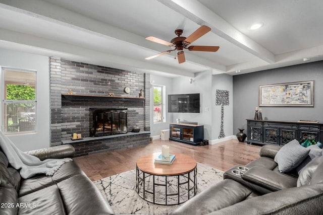 living area featuring a brick fireplace, wood finished floors, beam ceiling, and ceiling fan