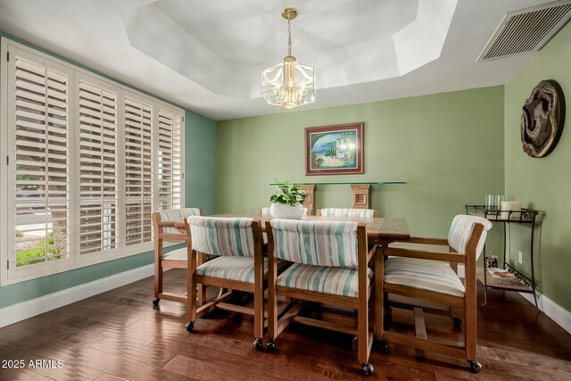 dining area with baseboards, an inviting chandelier, visible vents, a raised ceiling, and wood finished floors