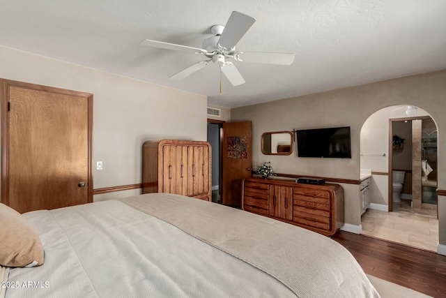 bedroom featuring visible vents, baseboards, arched walkways, ceiling fan, and wood finished floors