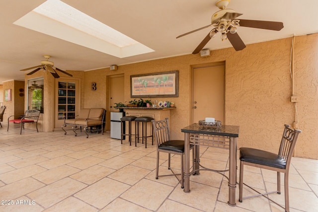 dining area featuring light tile patterned floors, a skylight, a ceiling fan, and a textured wall