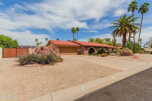 view of front of home with stucco siding, driveway, an attached garage, a tile roof, and fence