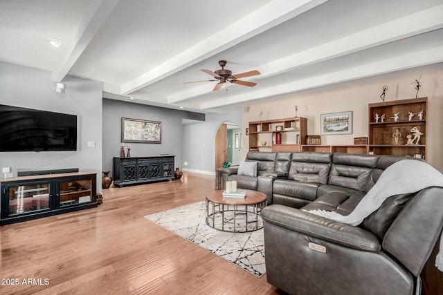 living area featuring baseboards, arched walkways, a ceiling fan, beam ceiling, and wood finished floors