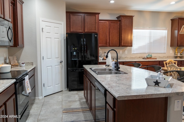 kitchen featuring light stone counters, an island with sink, sink, black appliances, and a kitchen bar