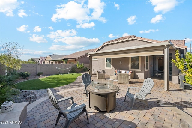 back of property with a yard, a patio, and an outdoor living space with a fire pit