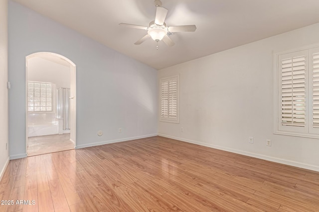 unfurnished room featuring arched walkways, ceiling fan, light wood finished floors, lofted ceiling, and baseboards