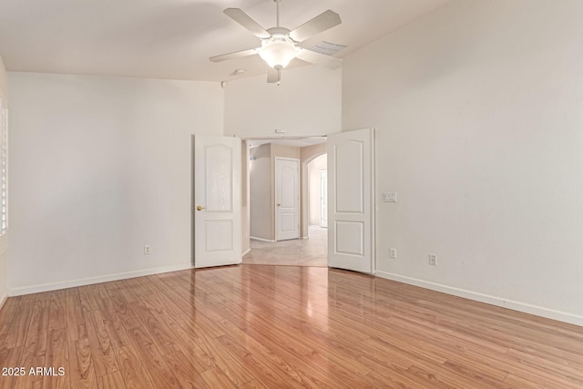 empty room featuring light wood-style floors, a ceiling fan, baseboards, lofted ceiling, and arched walkways