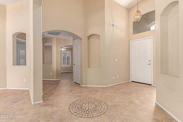 tiled foyer entrance with a high ceiling, baseboards, arched walkways, and a ceiling fan