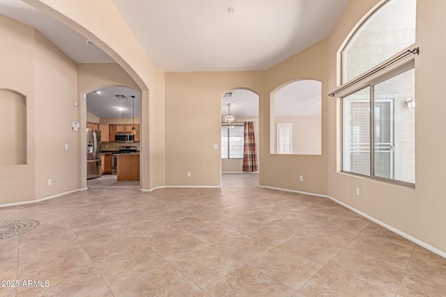 unfurnished room with light tile patterned floors, baseboards, and arched walkways