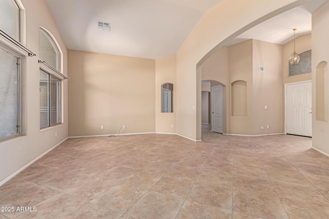 empty room with arched walkways, light tile patterned floors, baseboards, and a towering ceiling