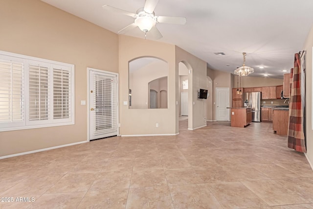 unfurnished living room featuring arched walkways, ceiling fan, baseboards, a chandelier, and lofted ceiling