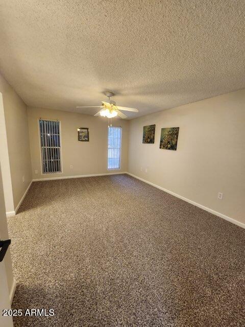 empty room featuring a textured ceiling, carpet flooring, baseboards, and ceiling fan