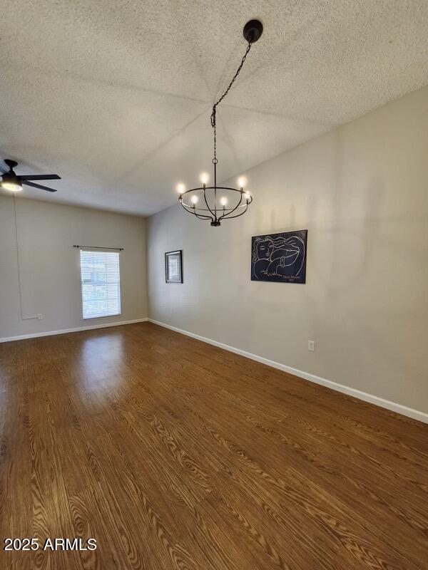 empty room featuring ceiling fan with notable chandelier, baseboards, a textured ceiling, and dark wood-style flooring