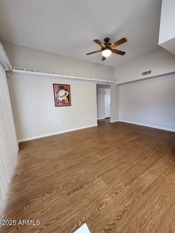 empty room with wood finished floors, a textured ceiling, ceiling fan, baseboards, and visible vents