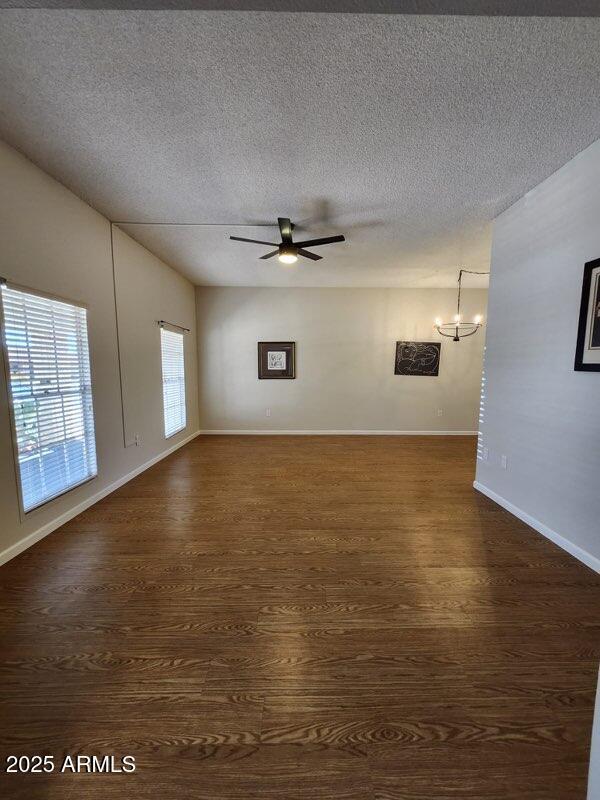 spare room with baseboards, a textured ceiling, dark wood-style floors, and ceiling fan with notable chandelier