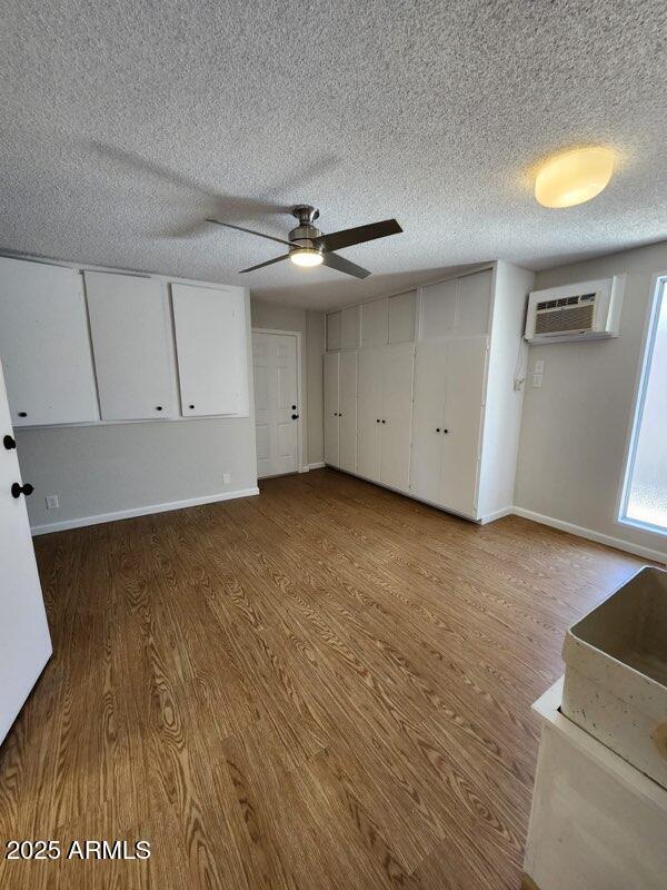 interior space featuring a wall mounted air conditioner, wood finished floors, a textured ceiling, ceiling fan, and baseboards