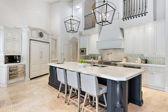 kitchen with a towering ceiling, a kitchen island with sink, sink, white cabinets, and stainless steel microwave