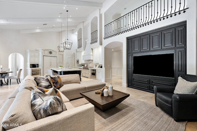 living room featuring a towering ceiling, beverage cooler, sink, beam ceiling, and a chandelier