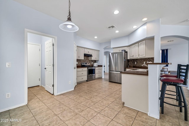kitchen with appliances with stainless steel finishes, arched walkways, dark countertops, a breakfast bar area, and under cabinet range hood