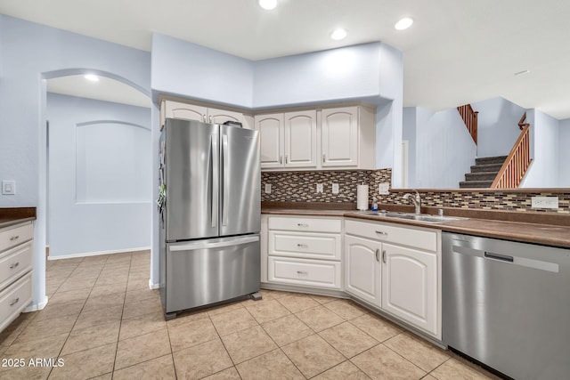 kitchen with appliances with stainless steel finishes, a sink, dark countertops, backsplash, and light tile patterned floors