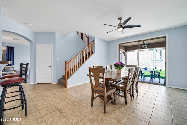 dining room featuring ceiling fan, light tile patterned floors, stairway, arched walkways, and baseboards