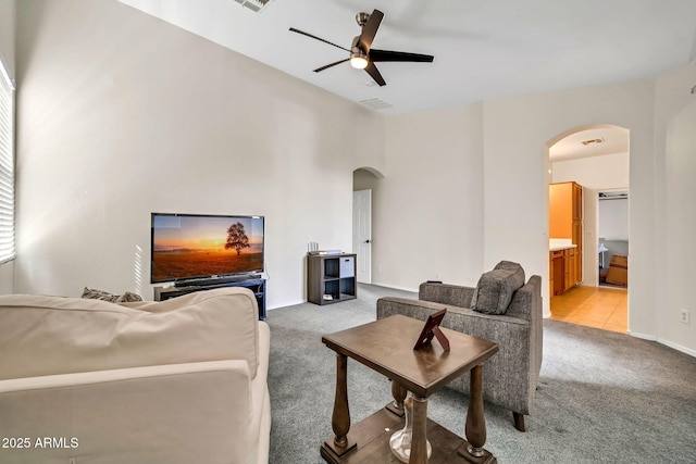 living area with arched walkways, a ceiling fan, light carpet, and baseboards