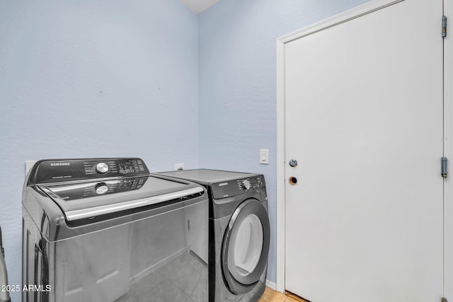laundry area featuring washer and clothes dryer, light tile patterned flooring, and a textured wall