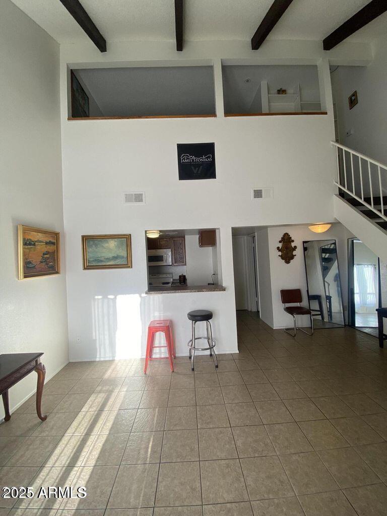 living area with a high ceiling, beamed ceiling, and tile patterned flooring