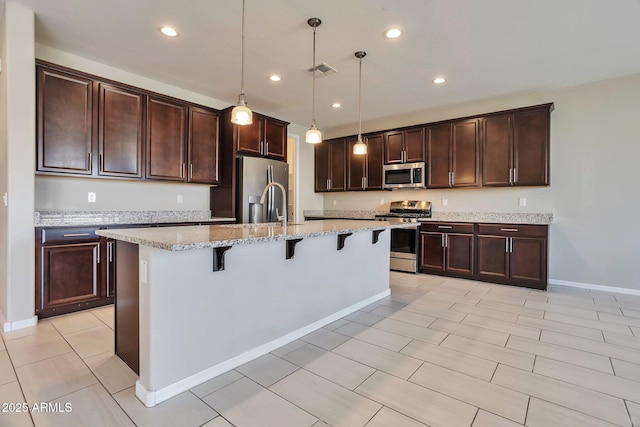 kitchen featuring a breakfast bar, light stone counters, decorative light fixtures, appliances with stainless steel finishes, and a kitchen island with sink