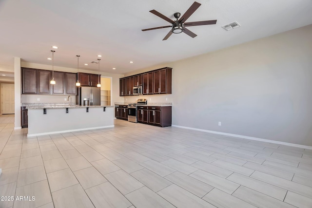 kitchen with a breakfast bar, sink, a center island with sink, appliances with stainless steel finishes, and pendant lighting