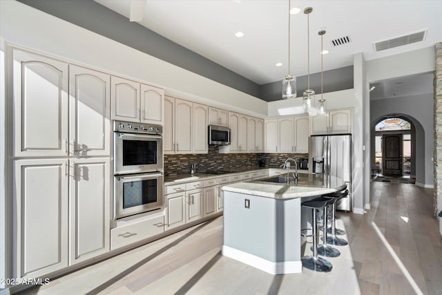 kitchen featuring pendant lighting, appliances with stainless steel finishes, decorative backsplash, a kitchen breakfast bar, and a kitchen island with sink