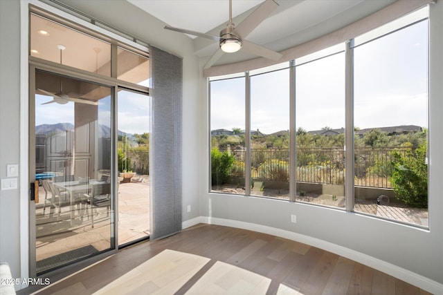 unfurnished sunroom featuring ceiling fan, a wealth of natural light, and a mountain view