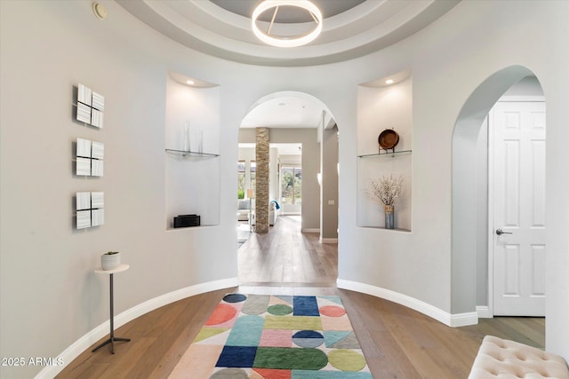 hallway featuring wood-type flooring, a towering ceiling, and a tray ceiling