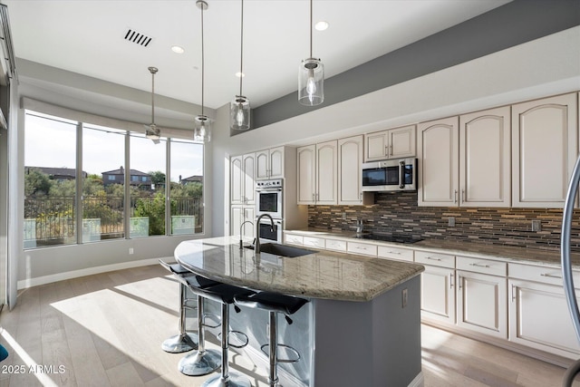 kitchen featuring pendant lighting, stainless steel appliances, dark stone counters, tasteful backsplash, and a kitchen island with sink