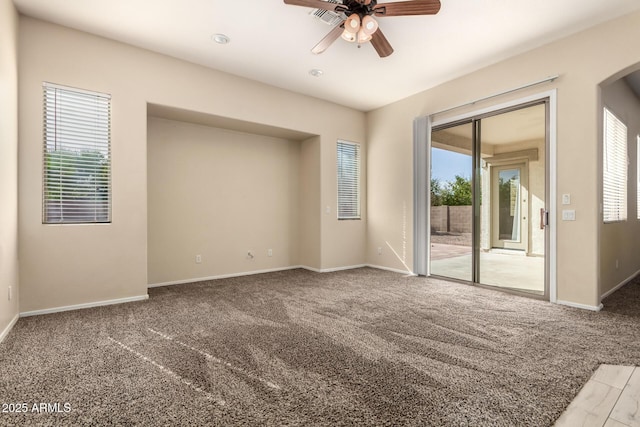 carpeted spare room featuring healthy amount of natural light, a ceiling fan, arched walkways, and baseboards