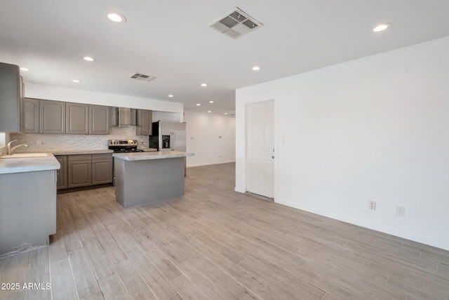 kitchen featuring appliances with stainless steel finishes, sink, wall chimney range hood, light hardwood / wood-style flooring, and a kitchen island