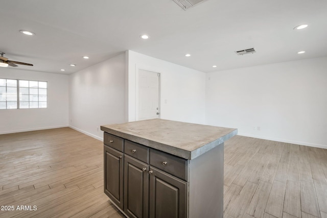 kitchen with ceiling fan, a kitchen island, dark brown cabinetry, and light hardwood / wood-style flooring