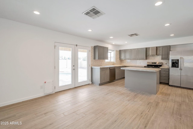 kitchen featuring a center island, french doors, wall chimney exhaust hood, gray cabinets, and stainless steel appliances