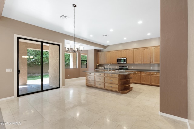 kitchen with an inviting chandelier, appliances with stainless steel finishes, a kitchen island with sink, hanging light fixtures, and sink