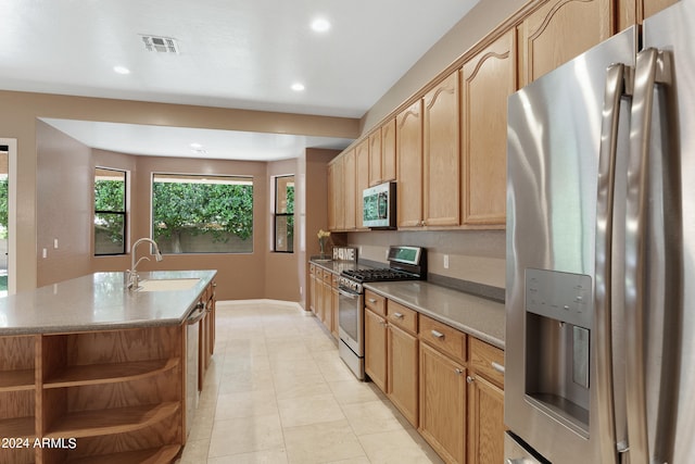 kitchen with light tile patterned floors, sink, appliances with stainless steel finishes, and a center island with sink