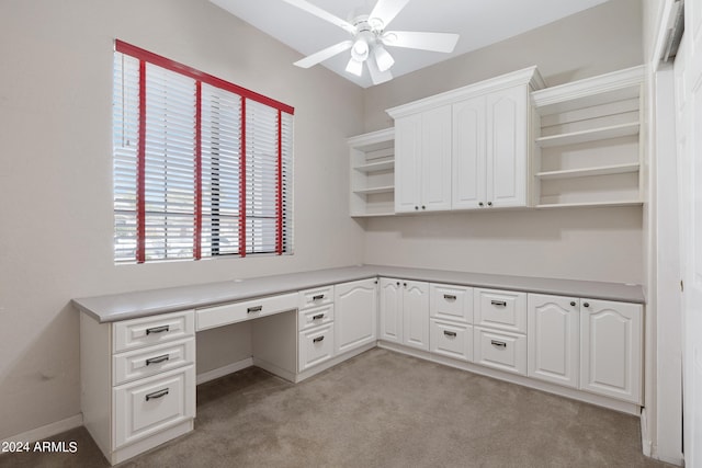 unfurnished office with ceiling fan, light colored carpet, and built in desk